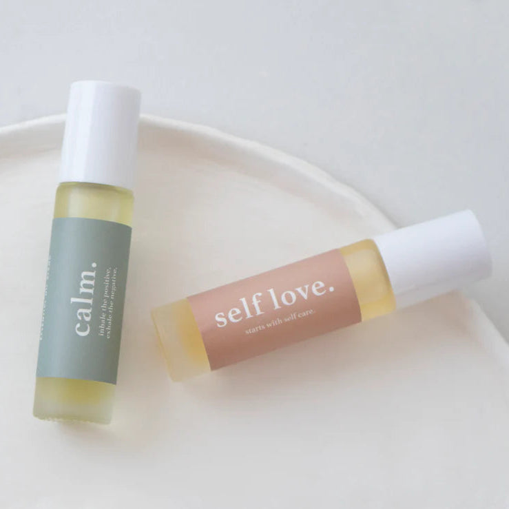 Two roller bottles labeled 'calm' and 'self love' on a white plate.