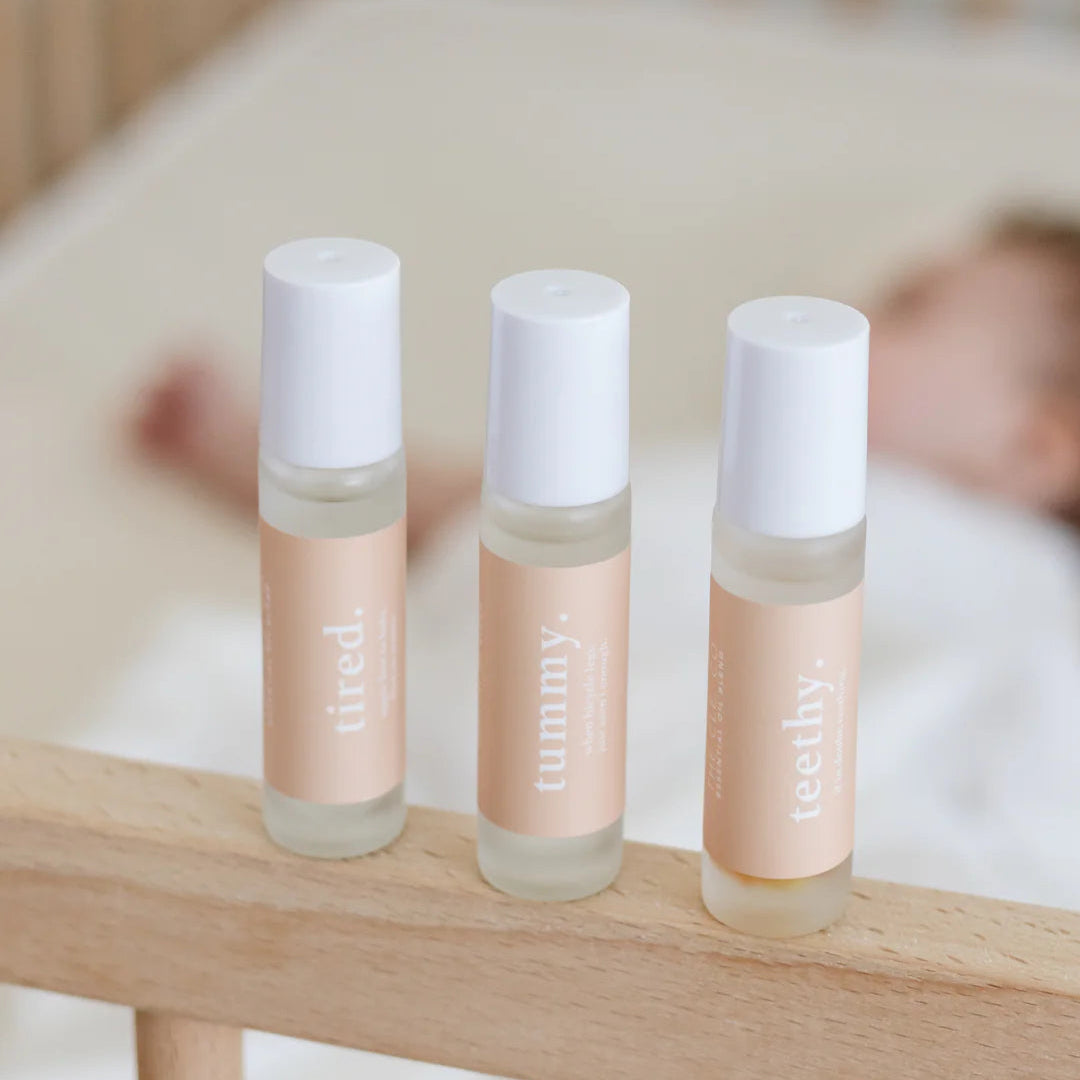 Three small bottles labeled 'tired', 'tummy', and 'teethy' on a wooden surface with a blurred background.