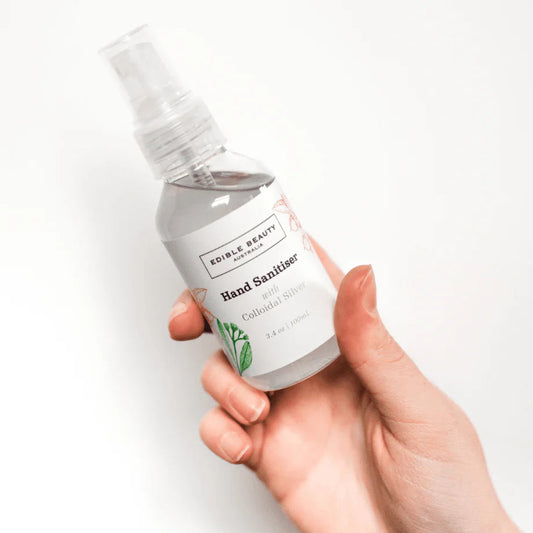 Hand holding a bottle of Edible Beauty hand sanitizer on a white background