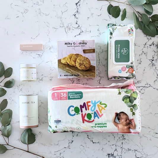 Omoiyari Baby Essentials Gift hamper box - nappies, bamboo baby wipes, lactation cookies, nursing tea, baby bum balm, essentials oil with green gum leaves on marble table.