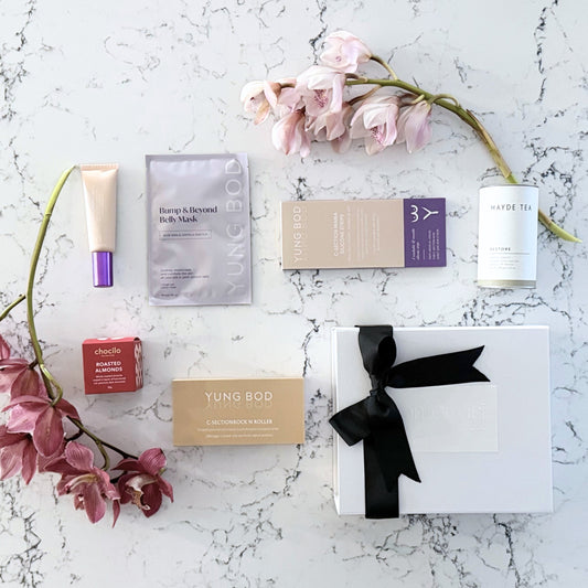 Omoiyari Caesarian Care gift hamper box - Organic healing tea, C-Section Silicon strips, Scar cream, C-Section skin roller and roasted almonds chocolate with pink orchid flowers on a marble surface