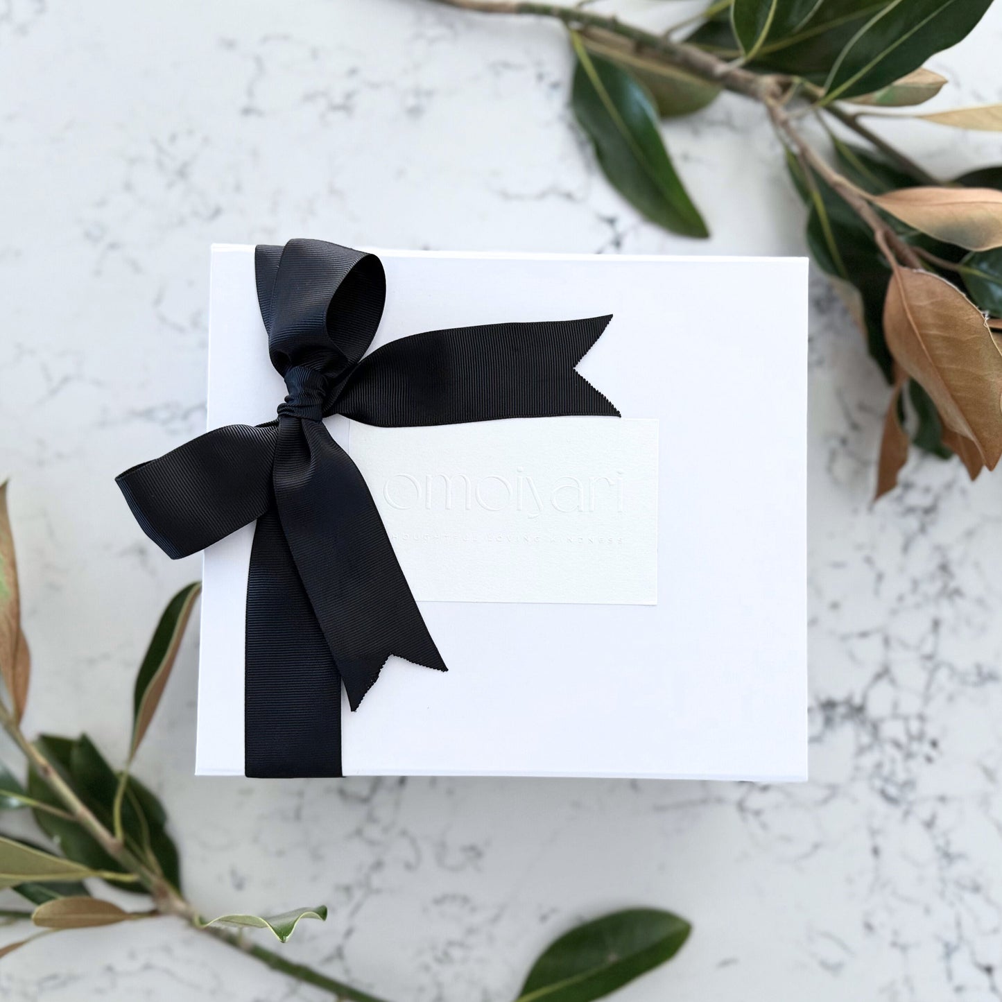Omoiyari gift hamper box with an Omoiyari label and black bow tie ribbon