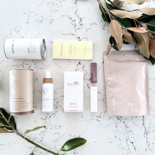 Omoiyari Nurture & Nourish Luxe gift hamper box - Skincare products, organic cacao and tea, pregnancy chocolate, stretch mark oil, radiance body oil, lip balm and green magnolia leaves on a marble surface