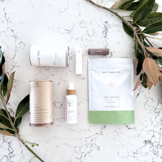 Omoiyari Nurture & Nourish gift hamper box - Skincare products, organic cacao and tea, stretch mark oil, lip balm and green magnolia leaves on a marble surface