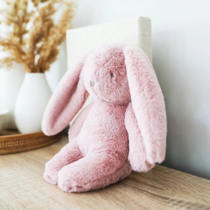 Pink plush bunny toy on a wooden surface with a decorative mirror and vase in the background.