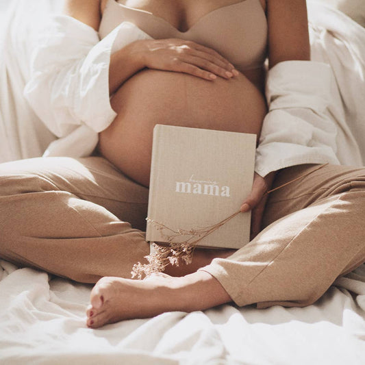 Pregnant person holding a book titled 'mama' with a soft, neutral color palette.