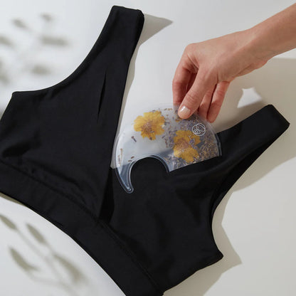 Black bralette top with a hand holding a clear silicone breast pad insert with floral design on a light background