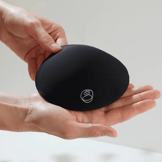 Person holding a black round breast pad with a Bare Mum logo on a light background