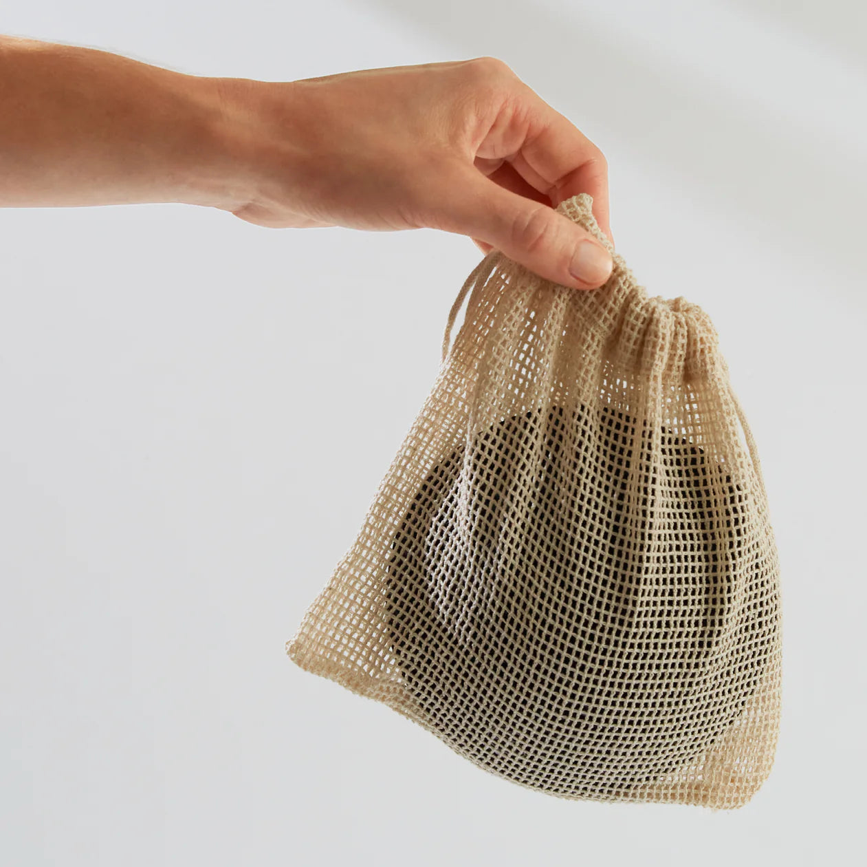 Hand holding a mesh drawstring bag with a white background