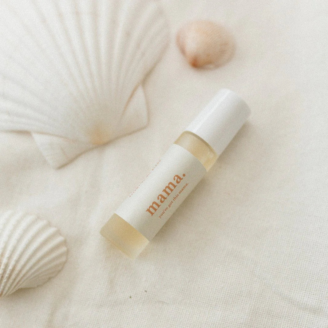 Skincare bottle labeled 'mama' on a textured beige surface with seashells.