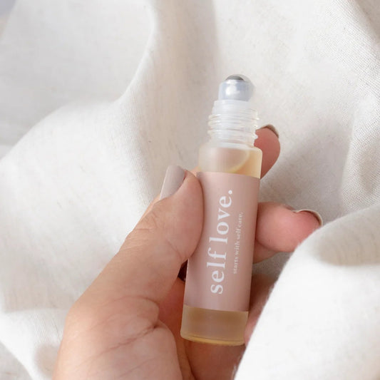 Hand holding a small bottle labeled 'self love' against a soft white background