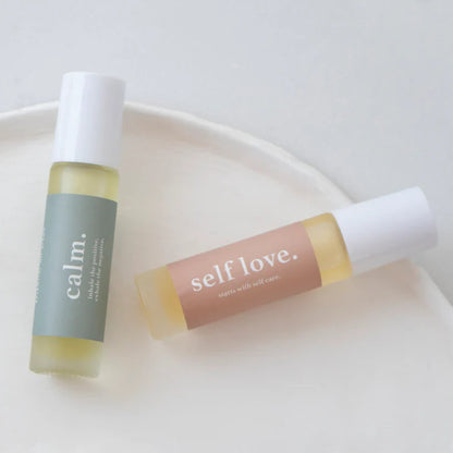 Two roller bottles labeled 'calm' and 'self love' on a white plate.