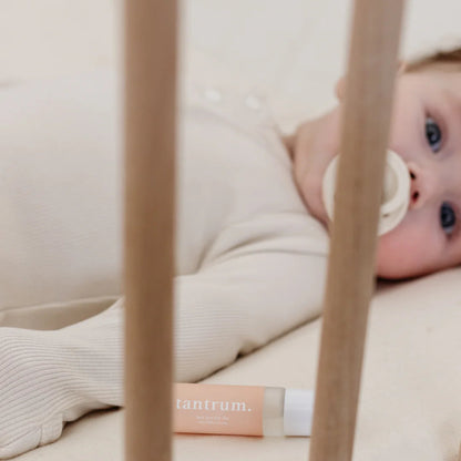 Baby lying in a crib with a pacifier, wearing a white outfit, and a 'tantrum' product visible.