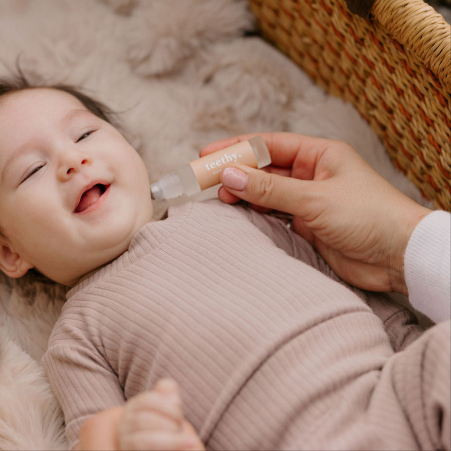 Baby lying in a crib with a hand holding a Cle Teethy Essentials Oil bottle