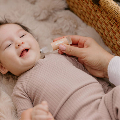 Baby lying in a crib with a hand holding a Cle Teethy Essentials Oil bottle