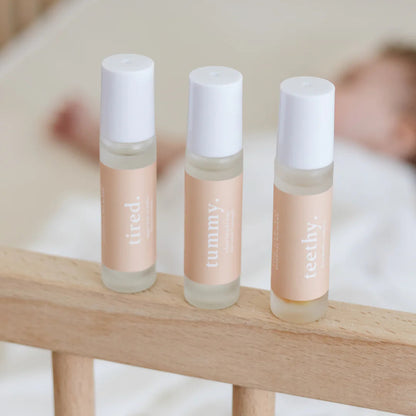 Three Cle Essential Oils Roller bottles labeled 'tired', 'tummy', and 'teethy' on a wooden surface with a blurred background.