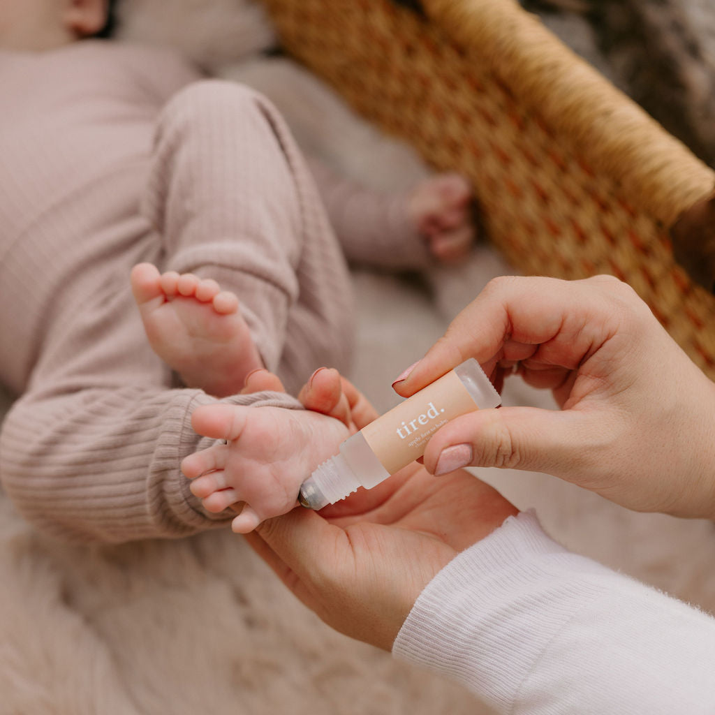 Mother applying Cle Tired Essentials Oil Roller to a child's foot in a cozy setting