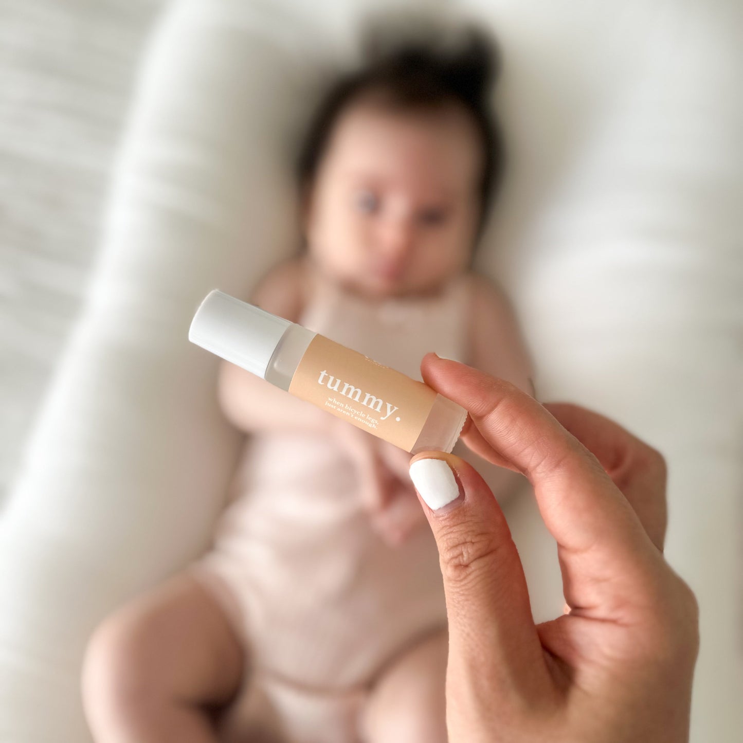Mother's hand holding a baby skincare product  Cle Tummy Essentials Oil roller bottle with a blurred baby in the background