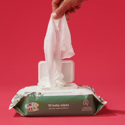 Hand pulling a baby wipe from a Comfy Koala baby wipes container against a red background