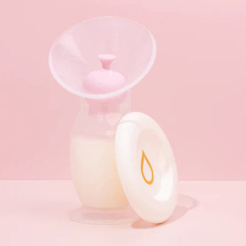 Manual breast pump with lids on a soft pink background