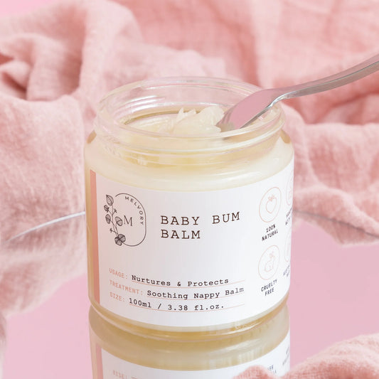 Jar of baby bum balm with a spoon inside on a pink background