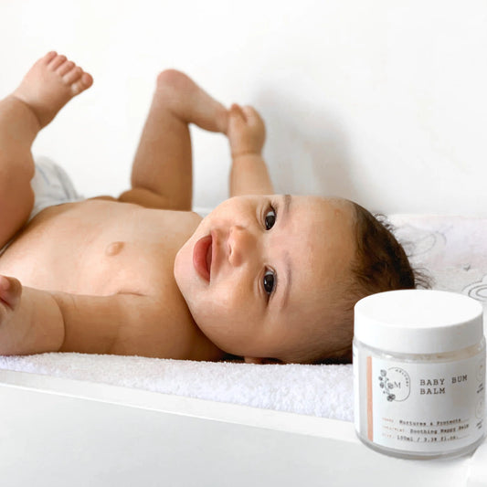 Baby lying on a white blanket with a jar of baby balm next to it.