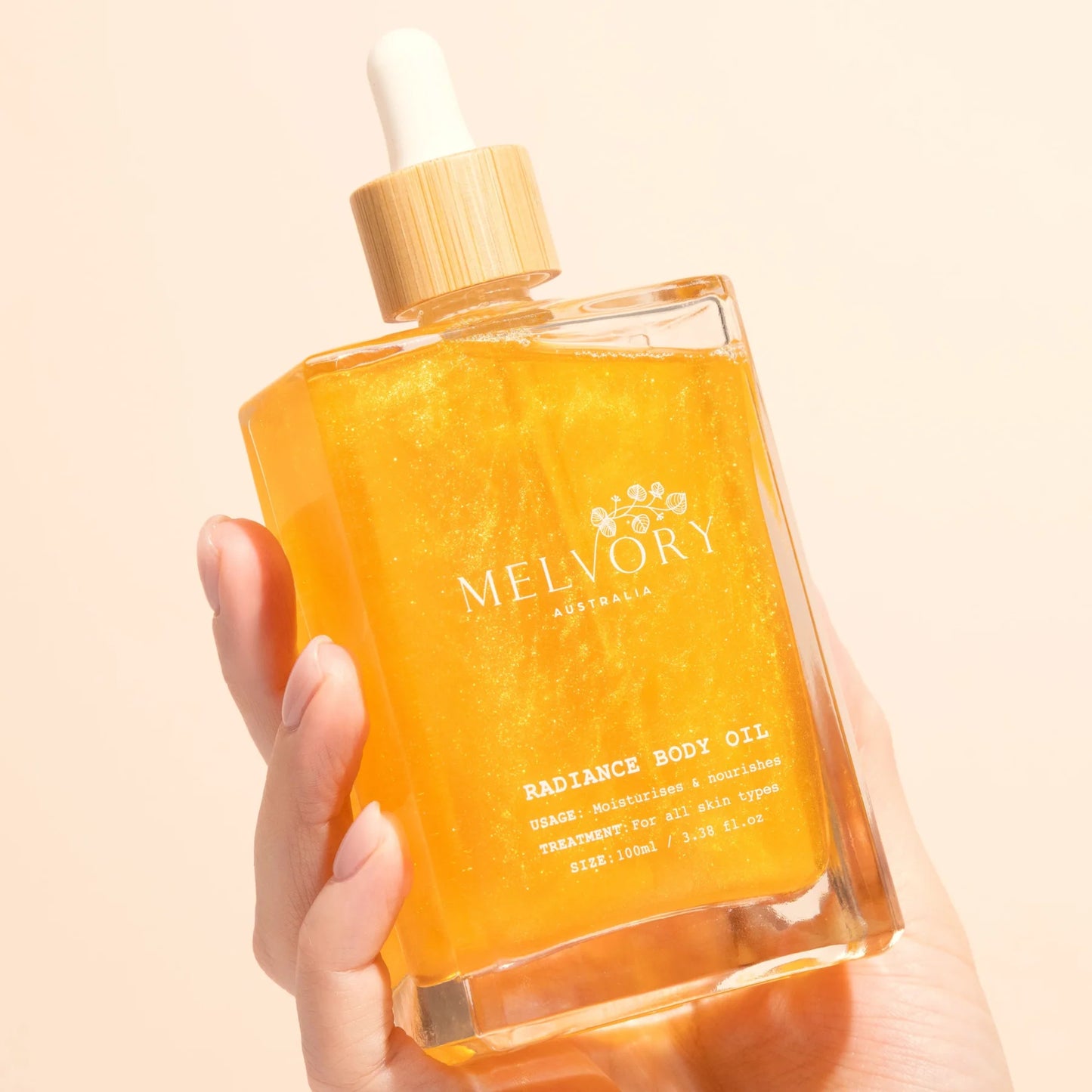 Hand holding a bottle of Melvory Radiance Body Oil against a beige background