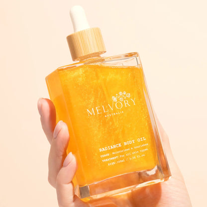Hand holding a bottle of Melvory Radiance Body Oil against a beige background