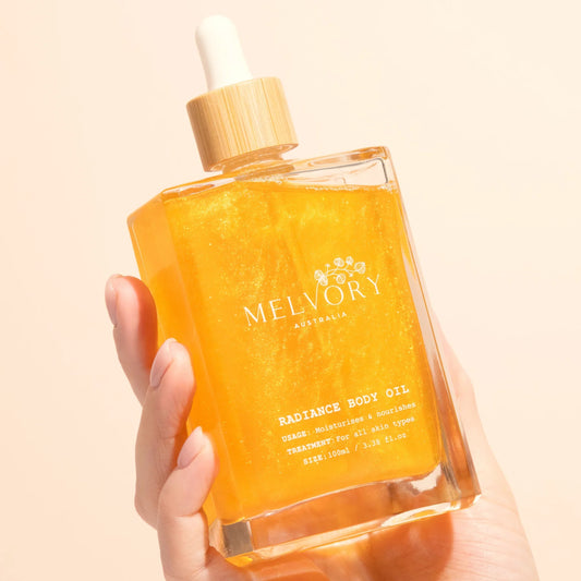 Hand holding a bottle of Melvory Radiance Body Oil against a beige background