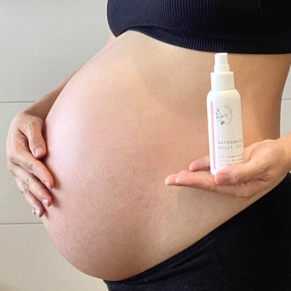 Pregnant belly with a hand holding a bottle of 'Watermelon Bellini' by The Honest Company.
