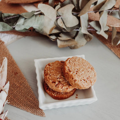 Two cookies on a square white plate with decorative leaves and fabric in the background