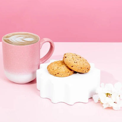 Pink mug with a coffee drink and cookies on a pink background