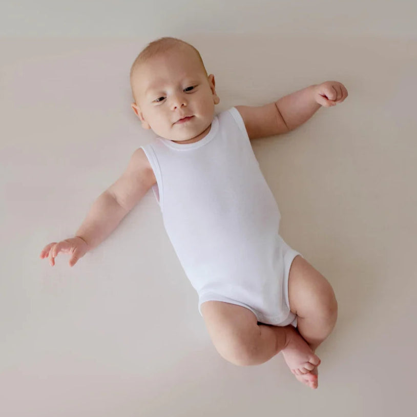 Baby in a white bodysuit onesie lying on a light pink surface