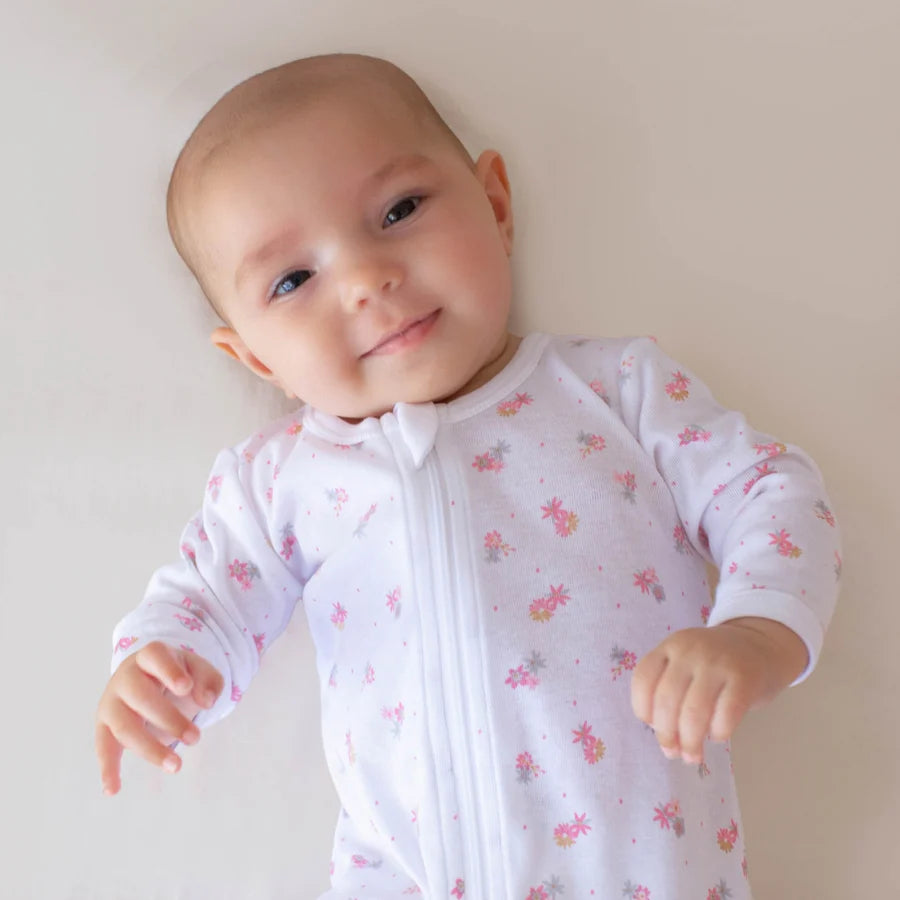 Baby wearing a white onesie with pink floral patterns on a plain background