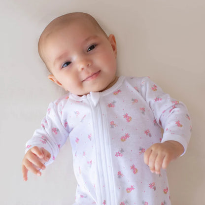 Baby wearing a white onesie with pink floral patterns on a plain background