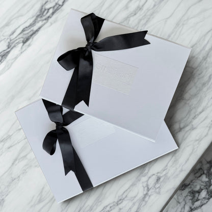 Two white Omoiyari gift hamper boxes with black ribbons on a marble surface