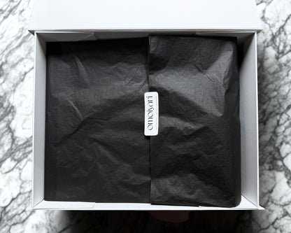 Black tissue paper in a white Omoiyari gift hamper box with a visible Omoiyari brand tag on a marble surface