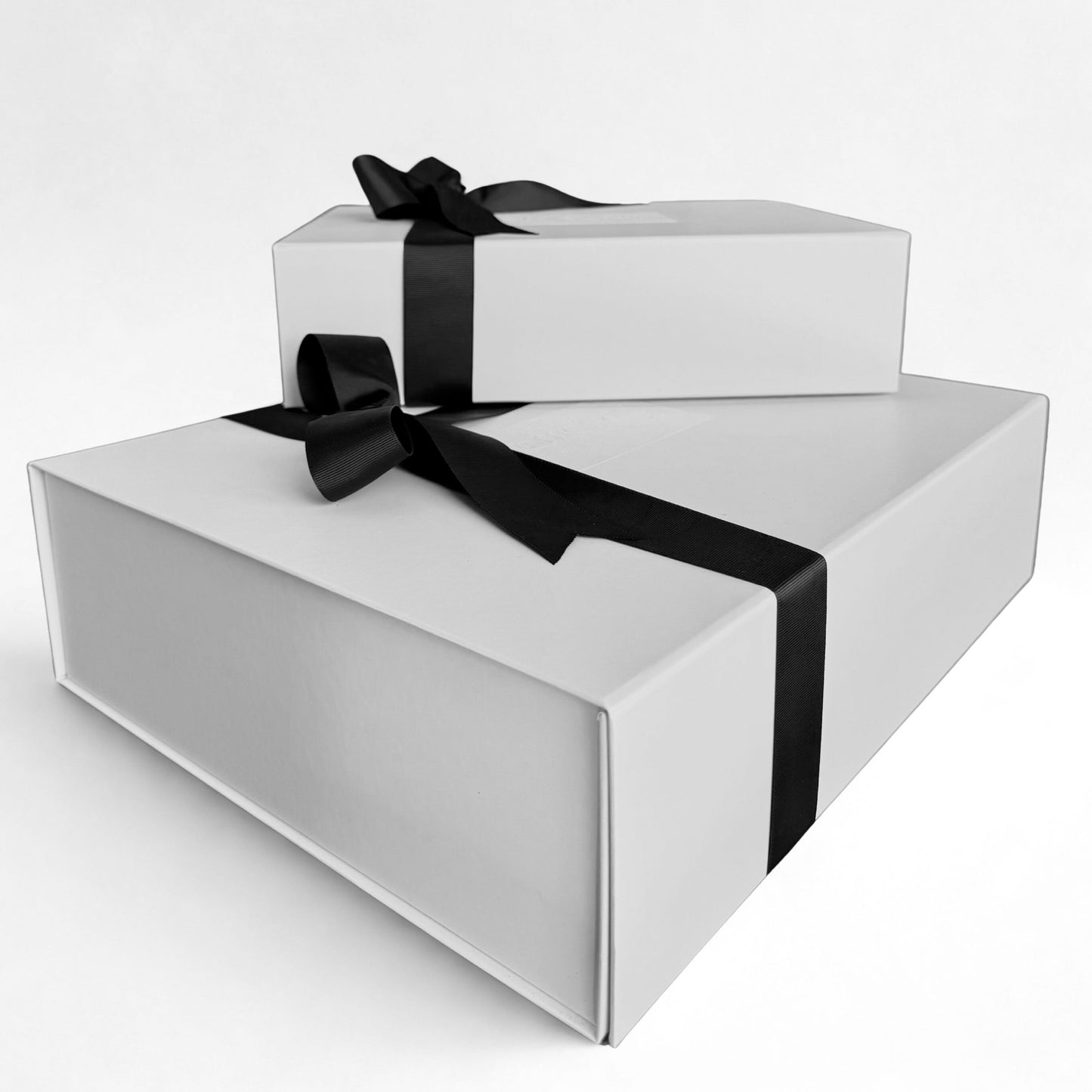 Two white Omoiyari gift hamper boxes with black ribbons on a light grey background