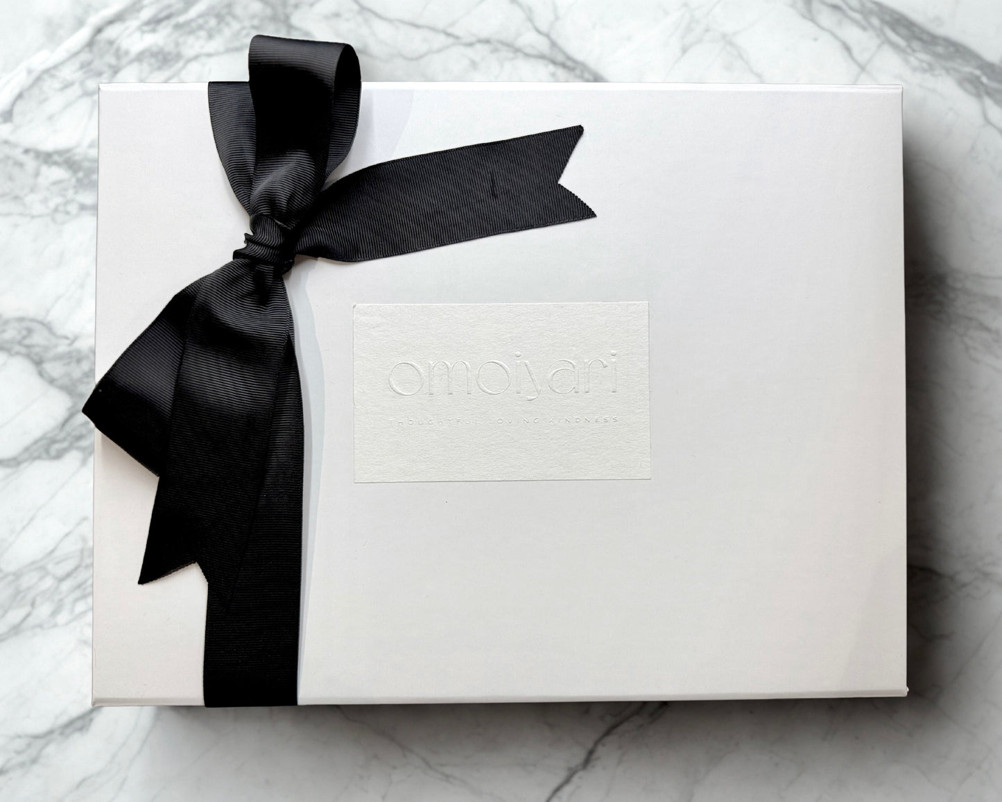 White Omoiyari gift box with a black ribbon on a marble surface