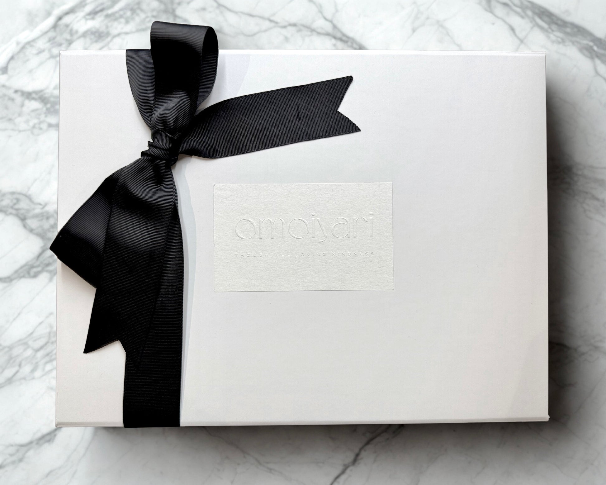 White Omoiyari gift box with a black ribbon on a marble surface