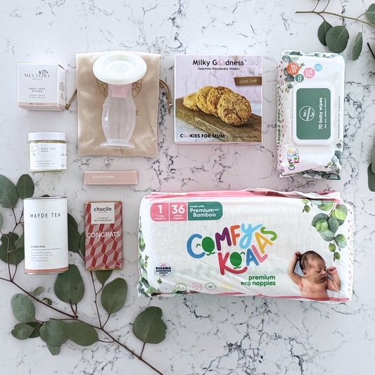 Omoiyari Baby Essentials Luxe Gift hamper box -  nappies, bamboo baby wipes, lactation cookies, chocolate, nursing tea, baby bum balm, essentials oil with green gum leaves on marble table.