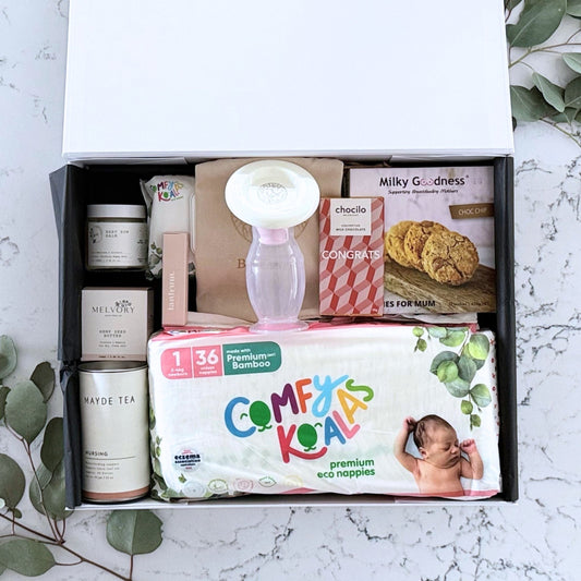 Omoiyari Baby Essentials Luxe Gift hamper box -  nappies, bamboo baby wipes, lactation cookies, chocolate, nursing tea, baby bum balm, essentials oil with green gum leaves on marble table.