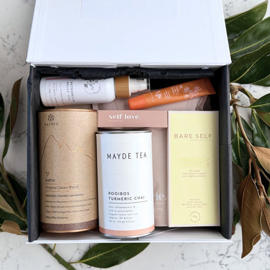 Omoiyari Glow & Grow Luxe gift hamper box - Skincare products, organic cacao and tea, mama pregnancy journal, pregnancy chocolate, stretch mark oil, lip balm and green magnolia leaves on a marble surface