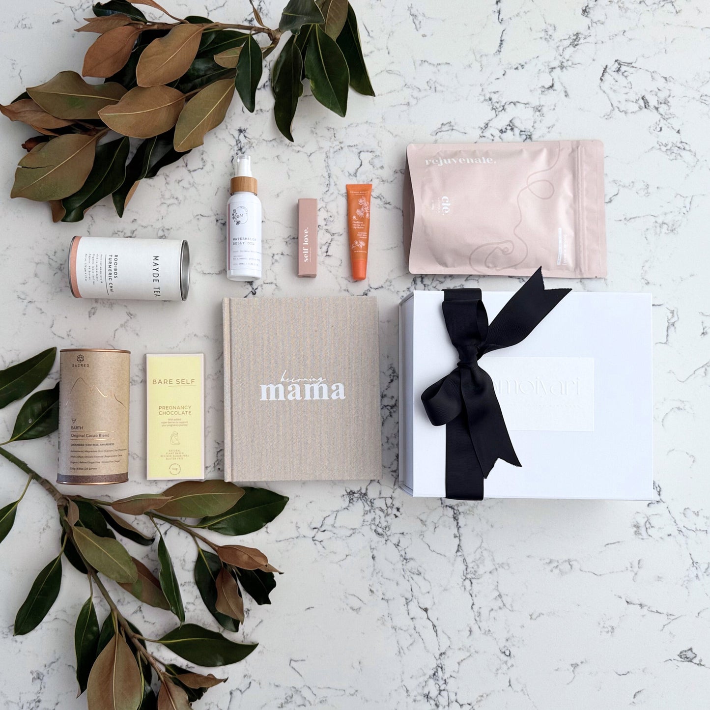 Omoiyari Glow & Grow Luxe gift hamper box - Skincare products, organic cacao and tea, mama pregnancy journal, pregnancy chocolate, stretch mark oil, lip balm and green magnolia leaves on a marble surface