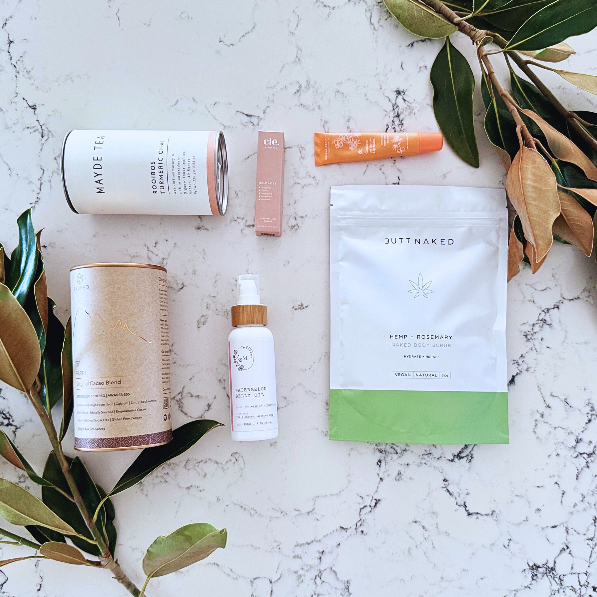 Omoiyari Glow & Grow gift hamper box - Skincare products, organic cacao and tea, stretch mark oil, lip balm and green magnolia leaves on a marble surface