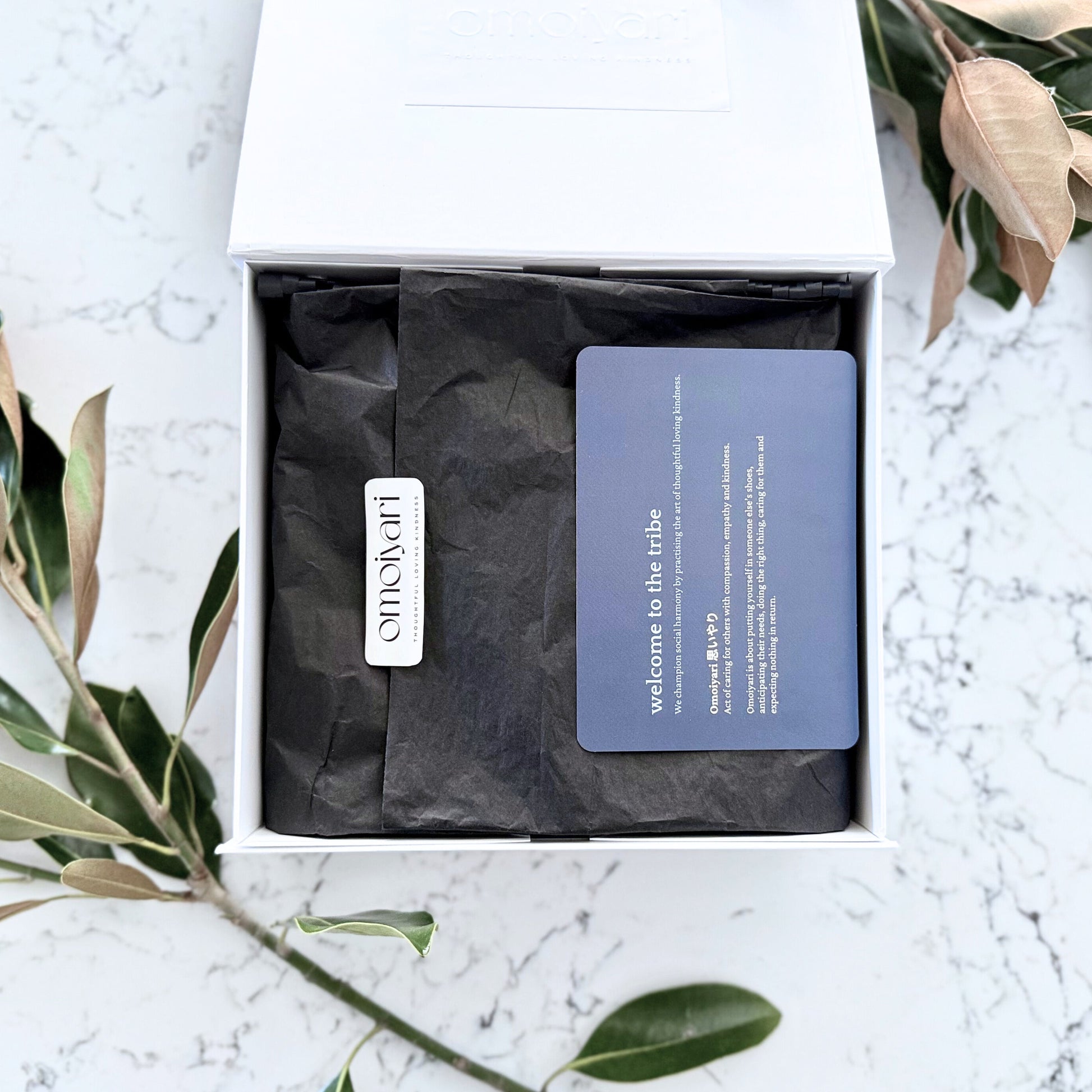 Omoiyari gift hamper box - lid is open and there is black tissue paper with an Omoiyari label sticker and welcome card