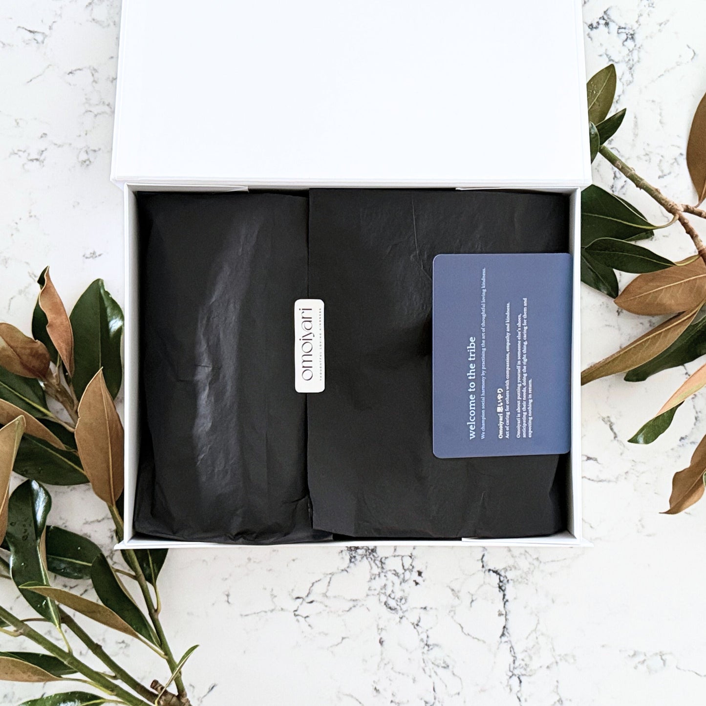 Omoiyari gift hamper box - lid is open and there is black tissue paper with an Omoiyari label sticker and welcome card