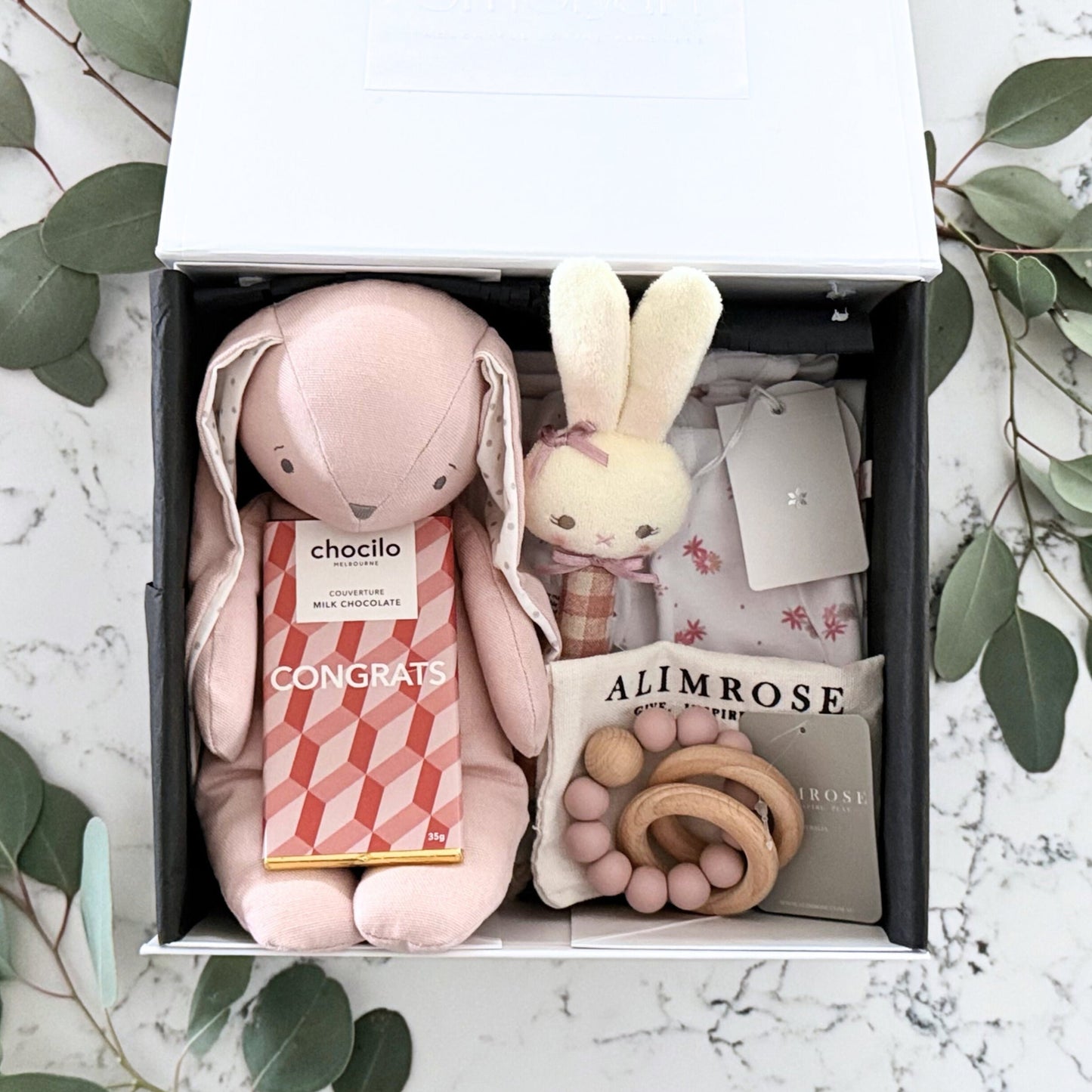 Omoiyari Hello Baby Girl Gift hamper box -  blue bunny plush toy, chocolate, Marquise growsuit, rattle and a teething ring with green gum leaves.