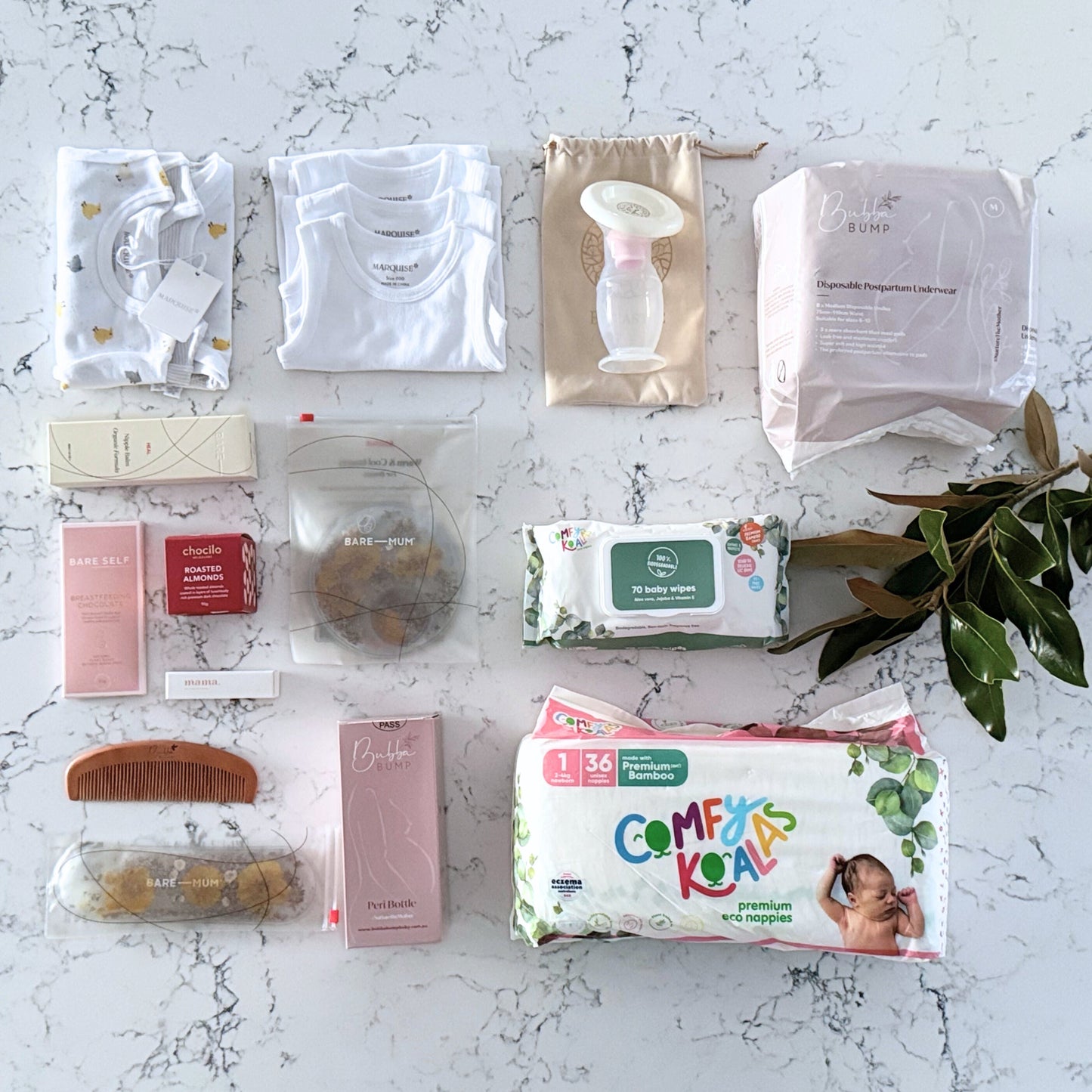 Omoiyari Hospital Bag Luxe gift hamper box with Marquise babywear, bamboo nappies and wipes, perineal bottle, nipple cream, Essentials Oils roller, Postpartum disposable underwear, bra cooling inserts and chocolate on a marble surface with flowers.
