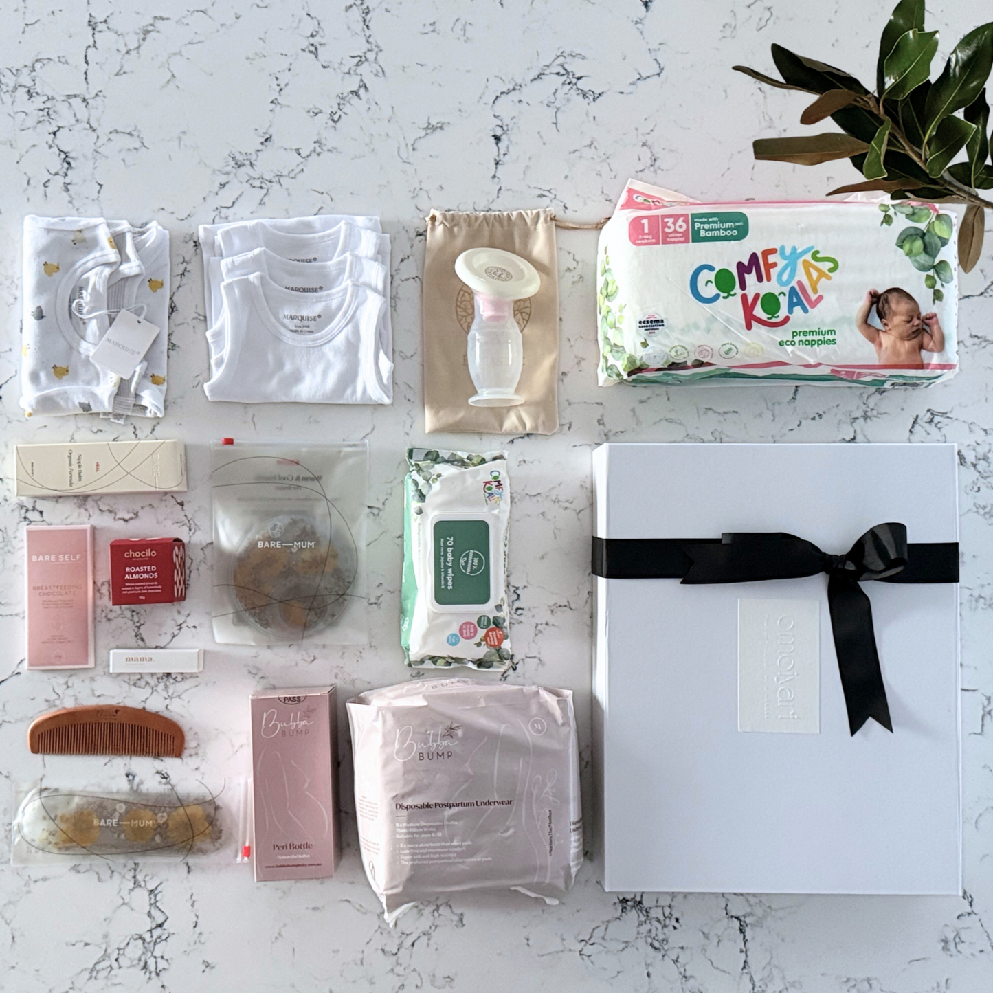 Omoiyari Hospital Bag Luxe gift hamper box with Marquise babywear, bamboo nappies and wipes, perineal bottle, nipple cream, Essentials Oils roller, Postpartum disposable underwear, bra cooling inserts and chocolate on a marble surface with flowers.